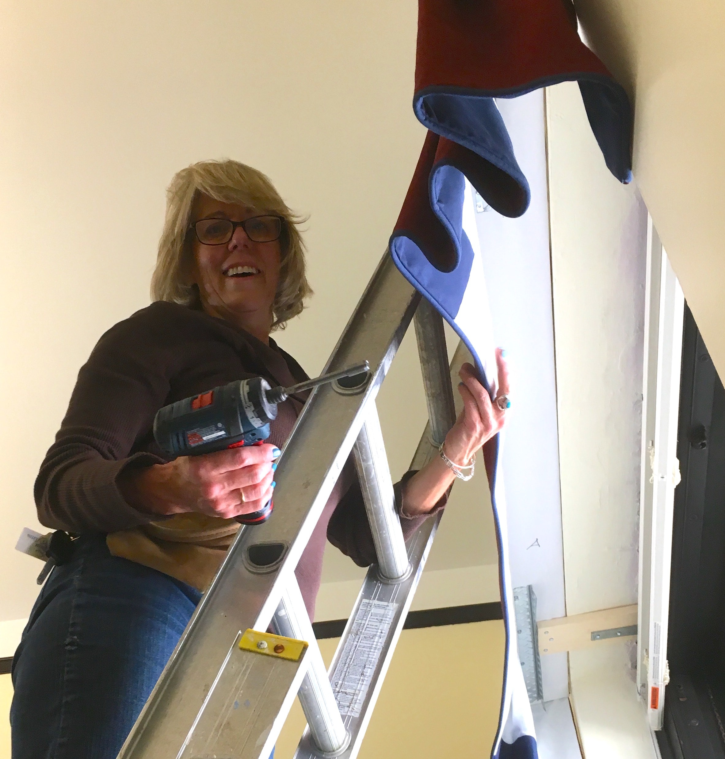 Heather installing window treatments on a ladder